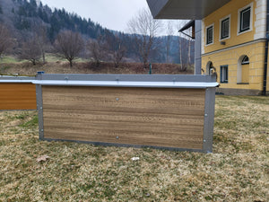 Leeres Hochbeet auf einer Wiese, vor einem Haus.