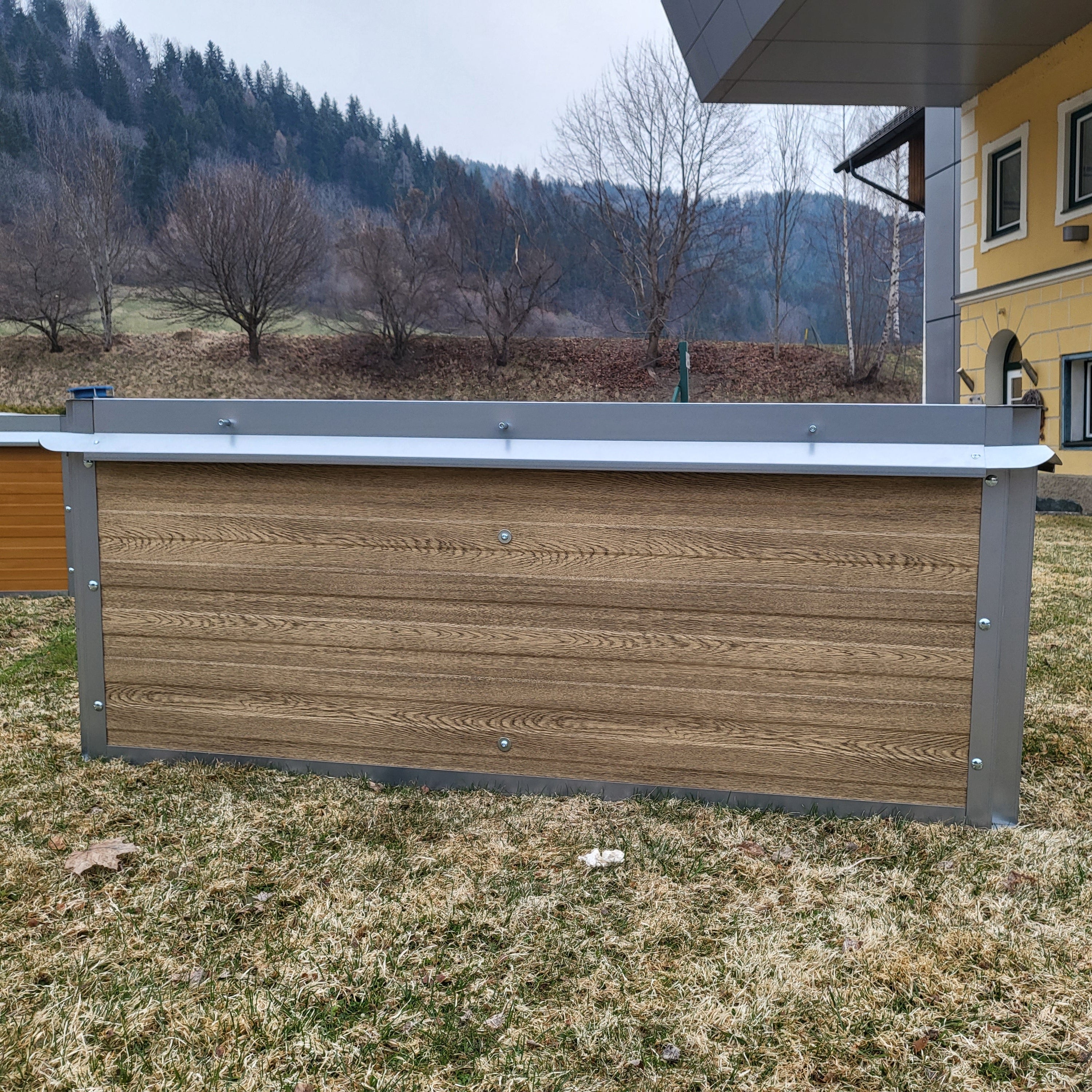 Leeres Hochbeet auf einer Wiese, vor einem Haus.