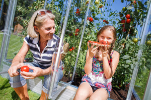 Frau & Mädchen sitzen am Tomatenhaus und essen Tomaten