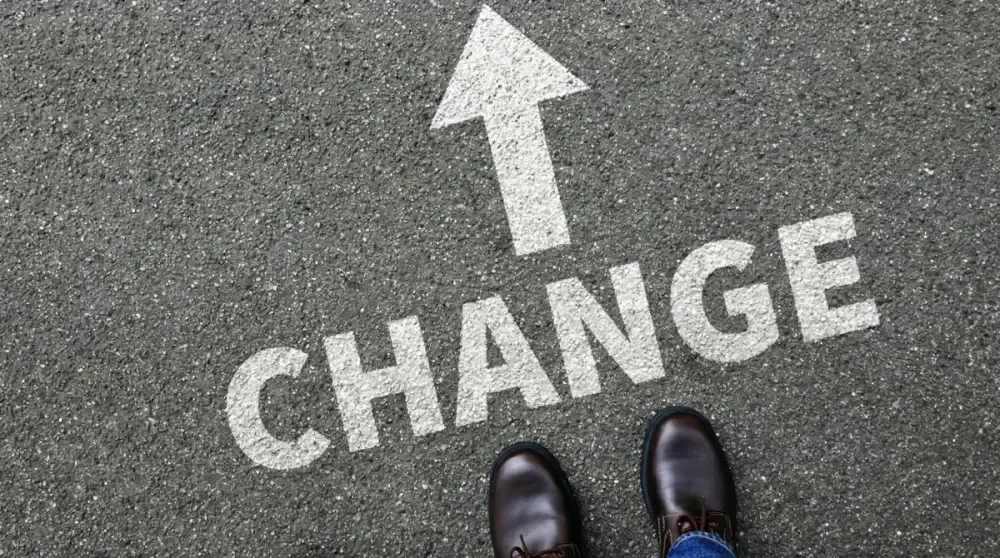 Schriftzug „Change" mit Pfeil auf Asphalt vor den Schuhen einer Person